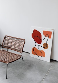 a wicker chair sits next to a painting